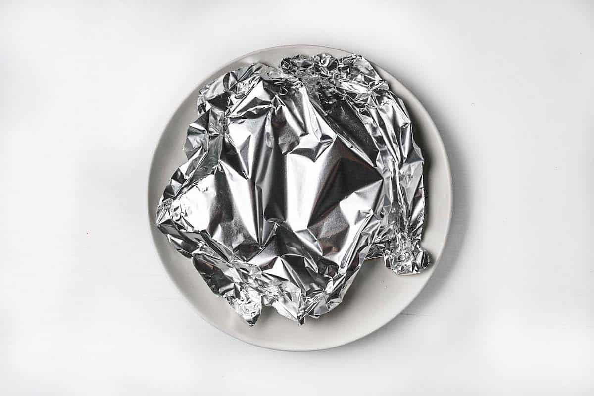 2 pork chops resting in foil on a white plate