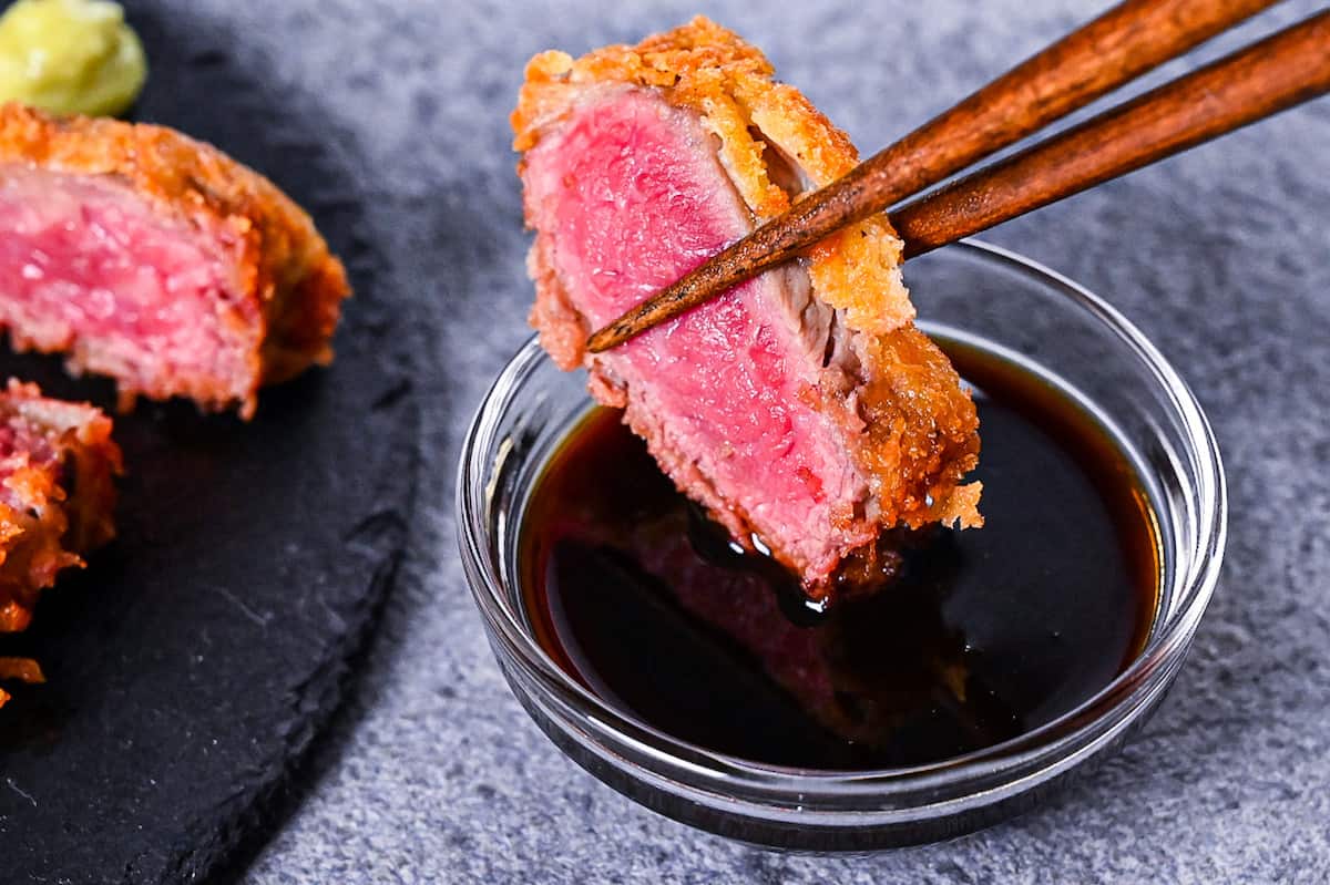 Gyukatsu (Japanese beef steak cutlet) served with cabbage, salt flakes and wasabi on a black slate plate