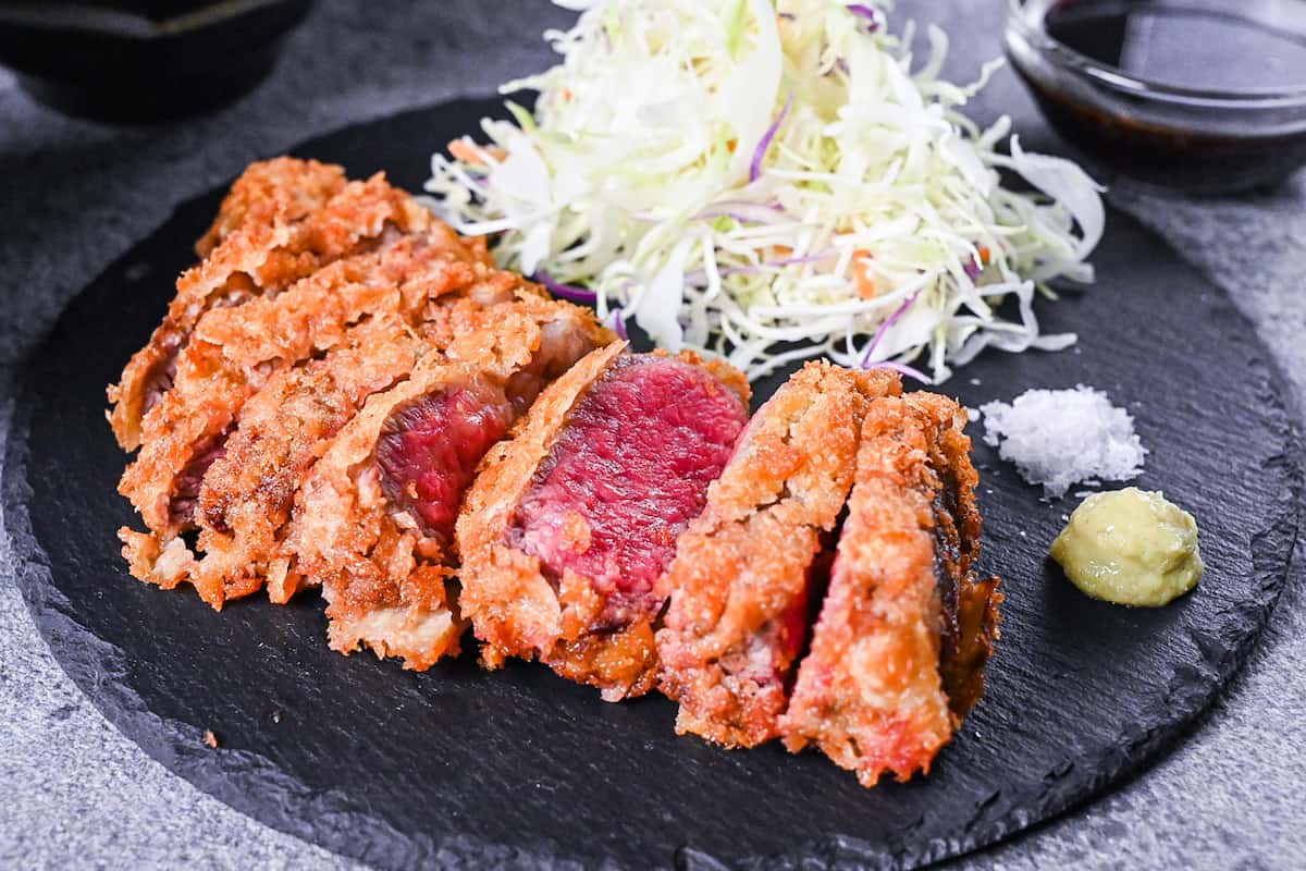 Gyukatsu (Japanese beef steak cutlet) served with cabbage, salt flakes and wasabi on a black slate plate