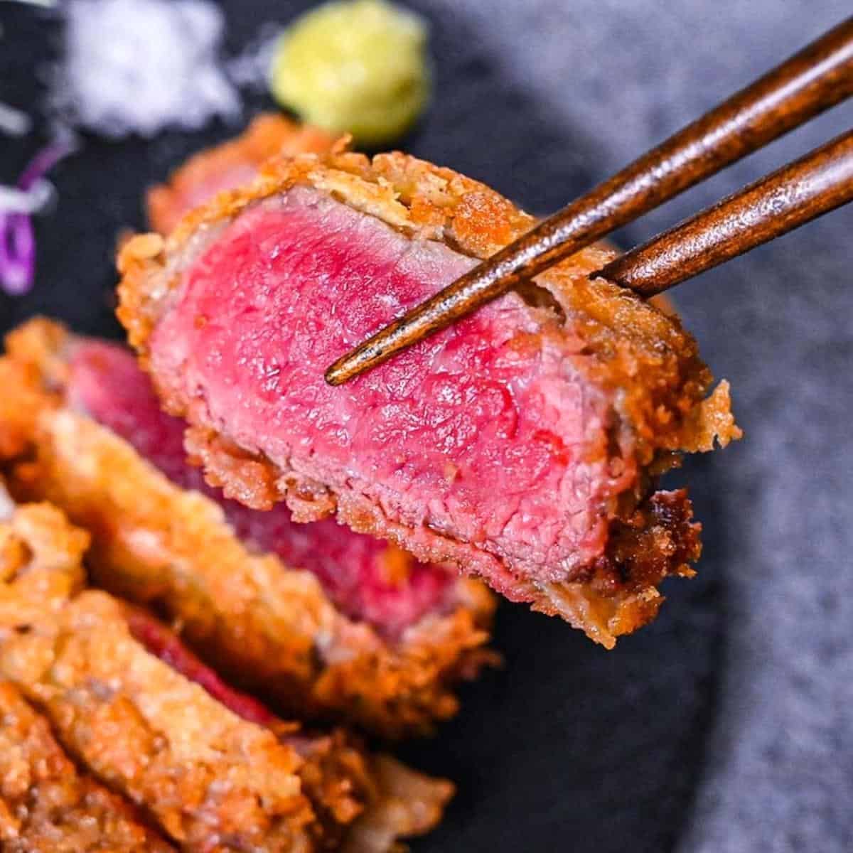 Gyukatsu (Japanese beef steak cutlet) served with cabbage, salt flakes and wasabi on a black slate plate