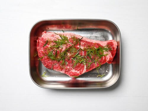 beef steak topped with fresh herbs in an aluminum container