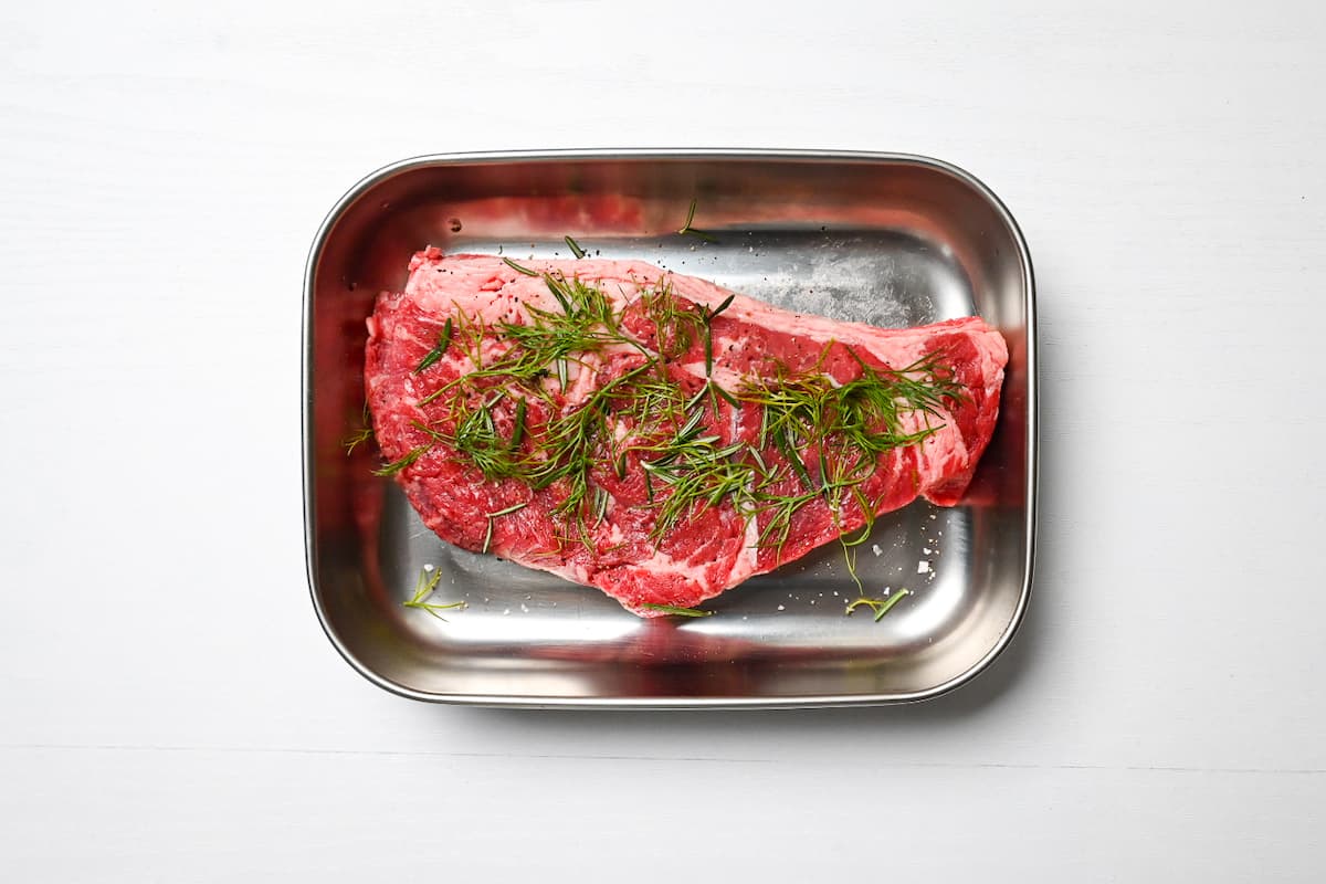 beef steak topped with fresh herbs in an aluminum container