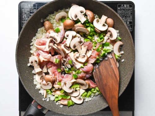 fried onion with chicken thigh, mushrooms and green bell peppers in a frying pan