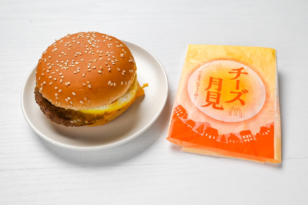 Japanese cheese tsukimi burger on a white plate next to yellow packaging