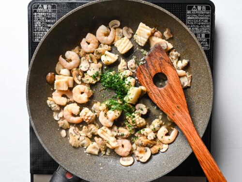 adding salt and parsley to stir fried mixed seafood