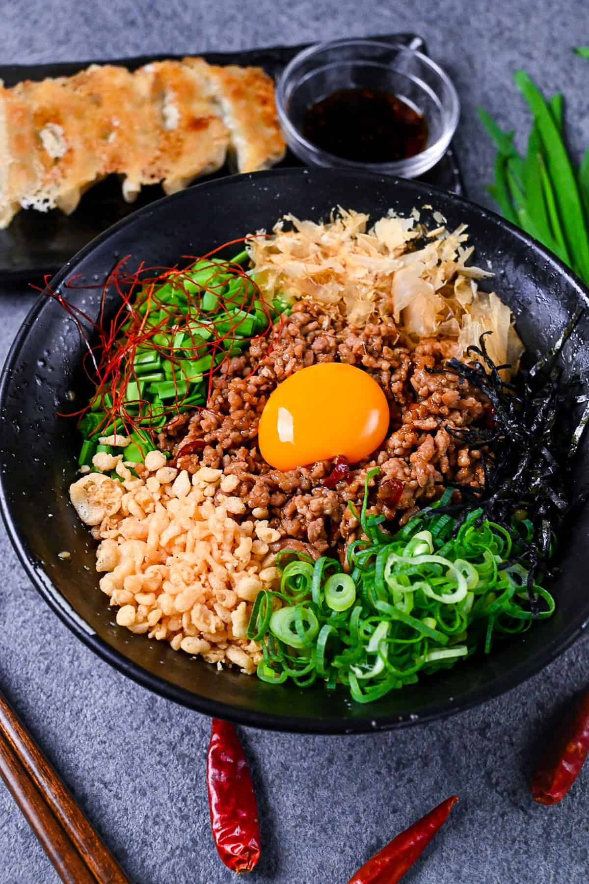 Taiwan Mazesoba served in a black ramen bowl and topped with seasoned pork mince, spring onions, Chinese chives, katsuobushi, tenkasu, kizami nori and a raw egg yolk