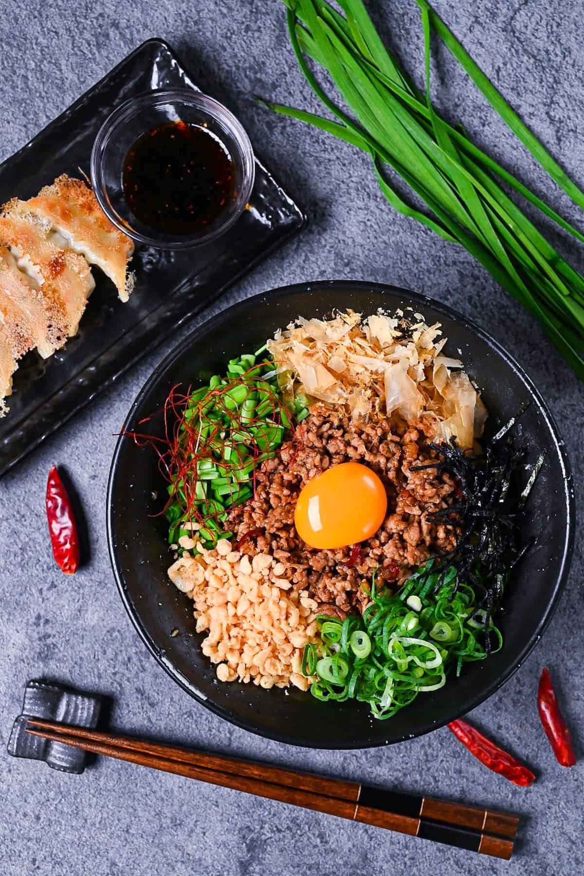 Taiwan Mazesoba served in a black ramen bowl and topped with seasoned pork mince, spring onions, Chinese chives, katsuobushi, tenkasu, kizami nori and a raw egg yolk