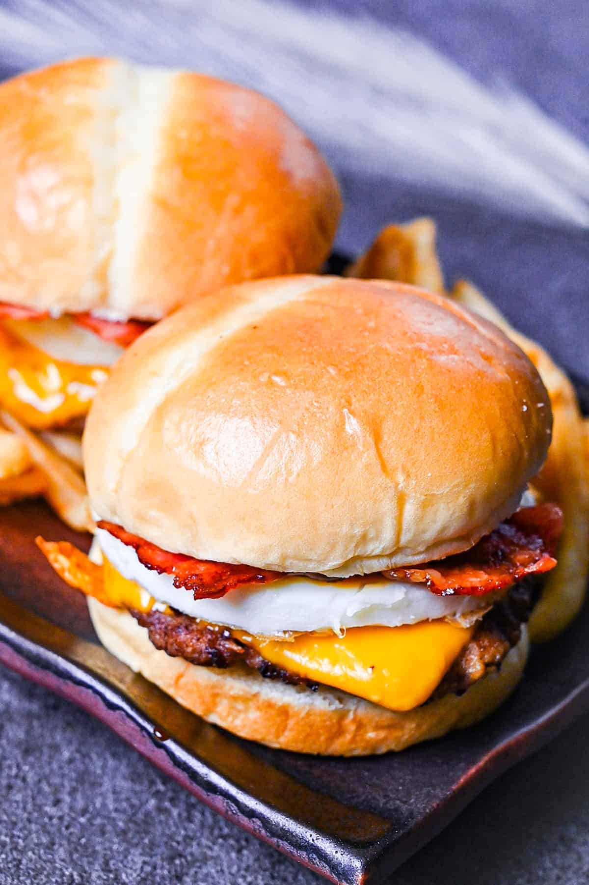 Japanese tsukimi burger on a brown rectangular plate with fries