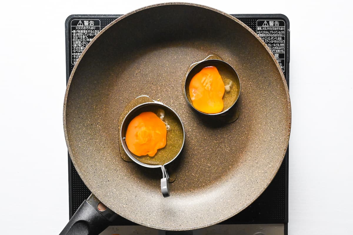 two eggs with broken yolks in molds in a frying pan
