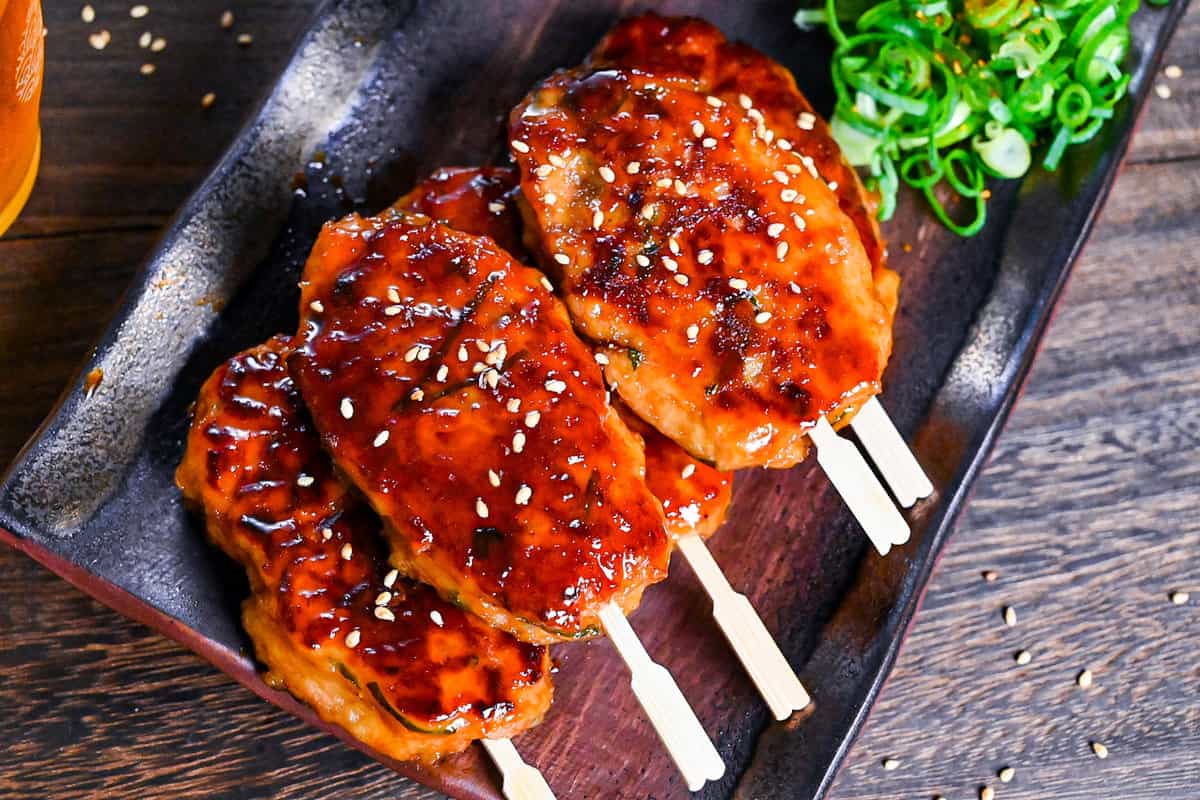 5 hand shaped chicken tsukune meatballs served on a rectangular plate with spring onion and raw egg yolk for dipping