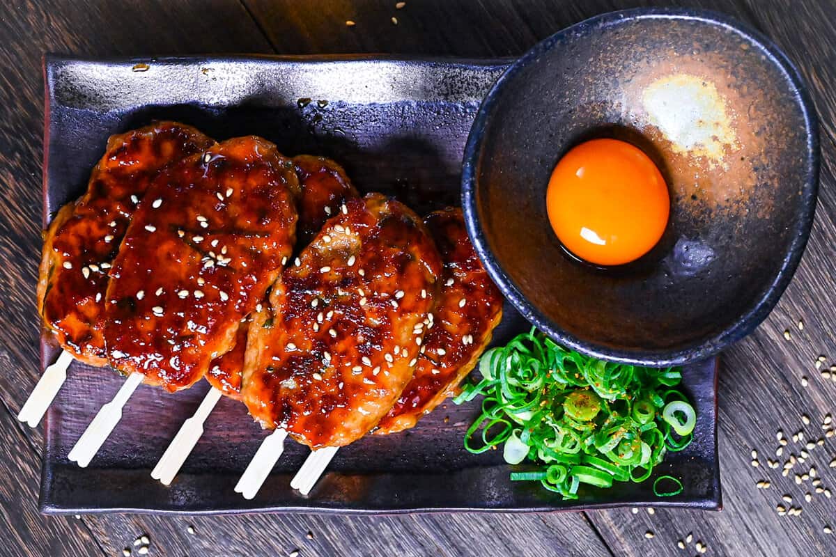 5 hand shaped chicken tsukune meatballs served on a rectangular plate with spring onion and raw egg yolk for dipping