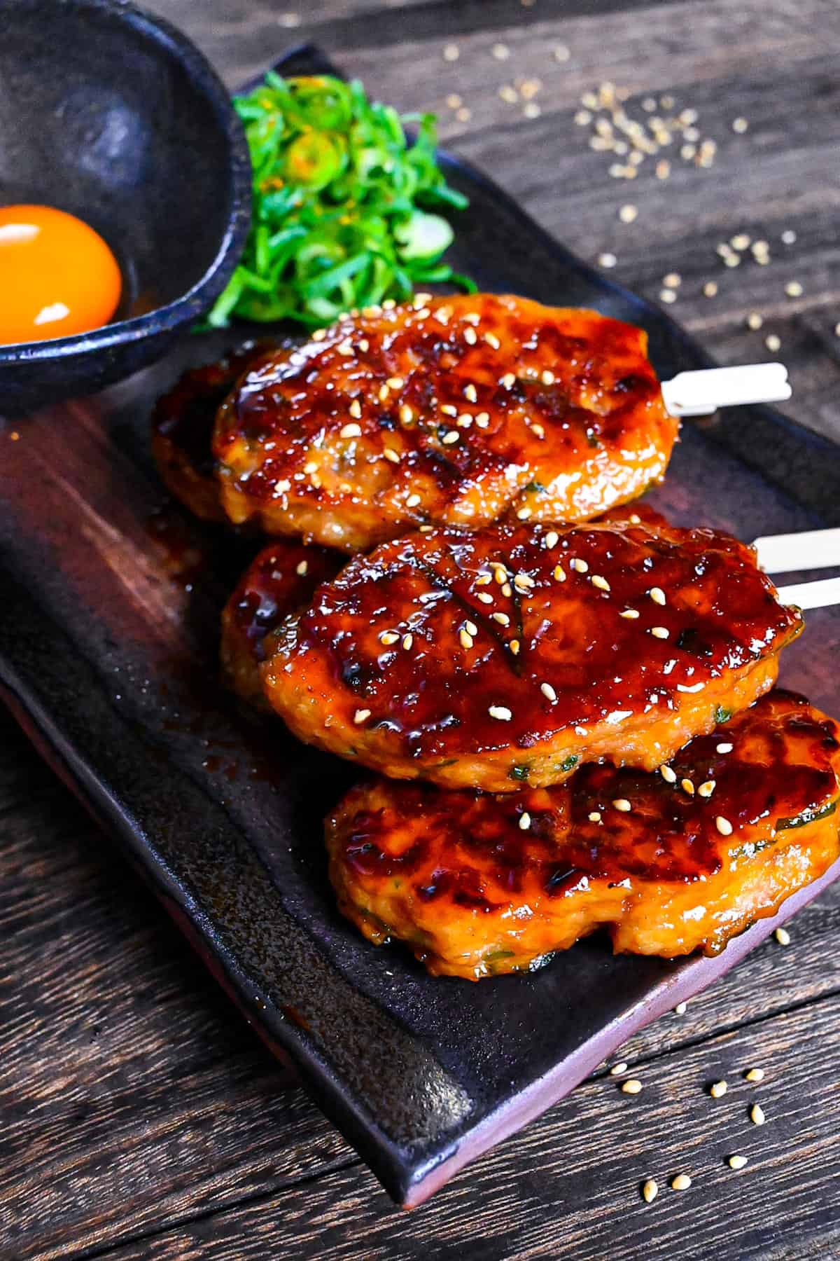 5 hand shaped chicken tsukune meatballs served on a rectangular plate with spring onion and raw egg yolk for dipping