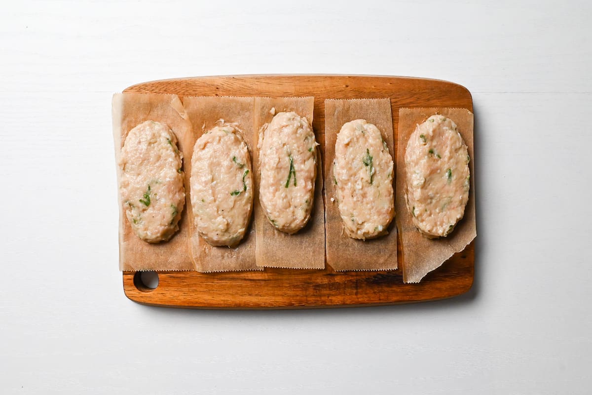 oblong shaped tsukune meatballs arranged on baking paper on a wooden chopping board