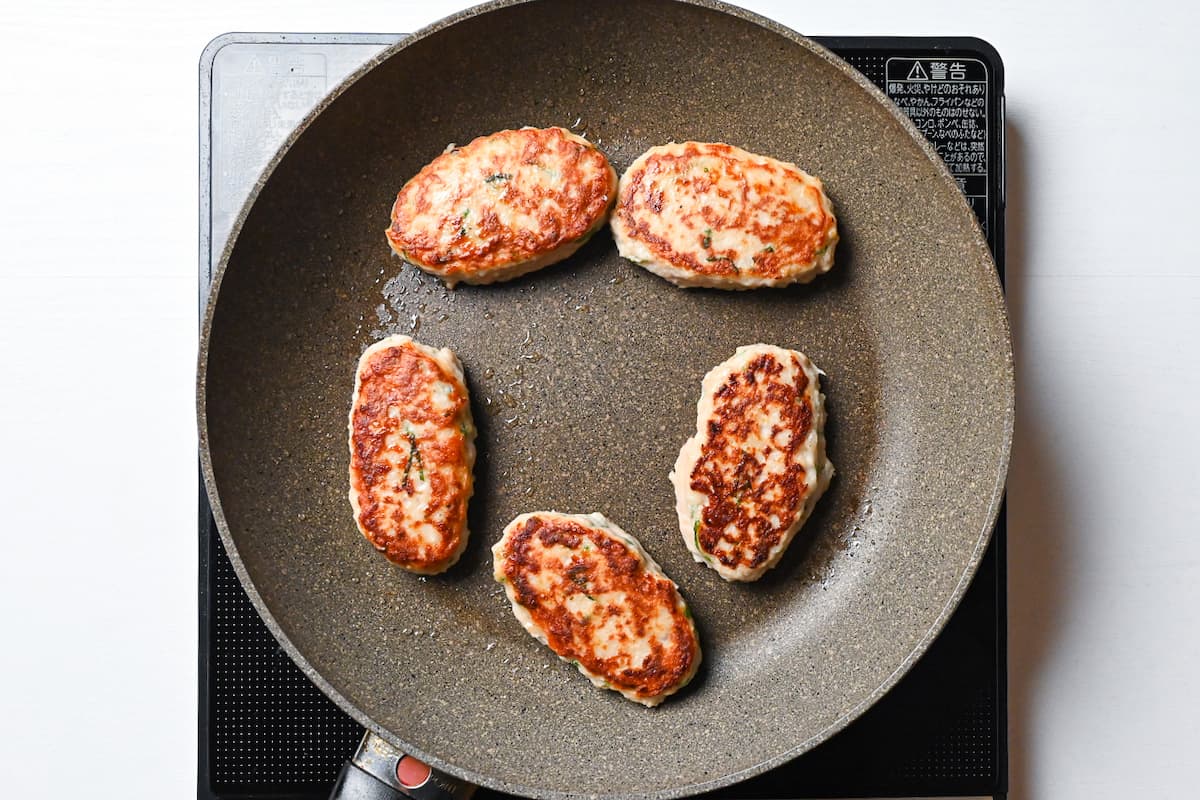 chicken tsukune browned on one side in a frying pan