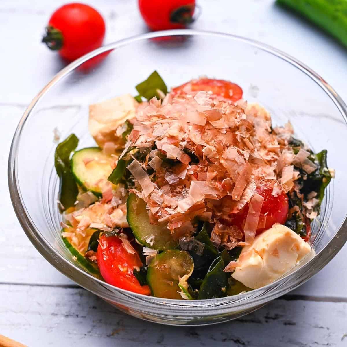 Japanese wakame seaweed salad made with tofu, cucumber and mini tomatoes in a small glass bowl