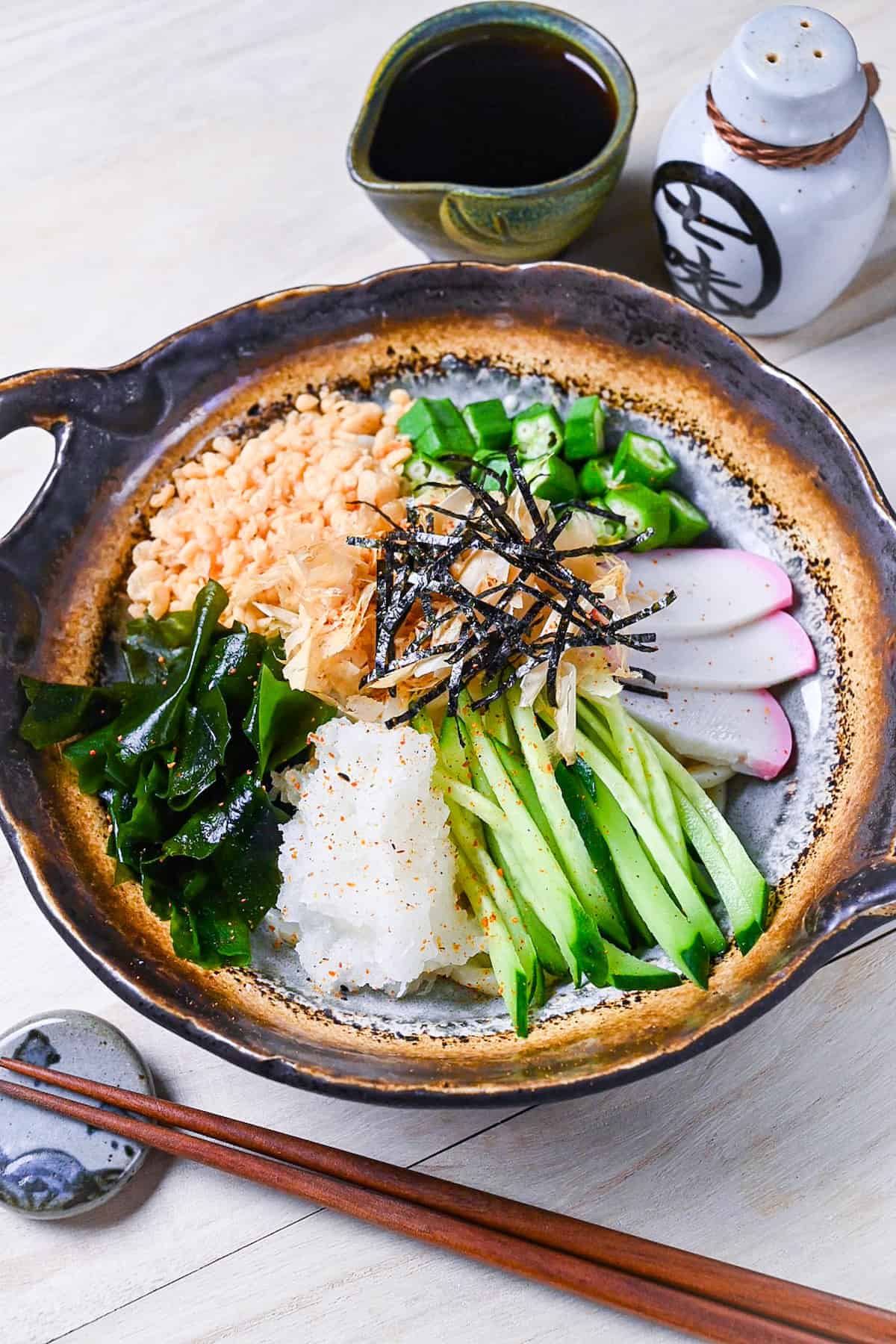 Hiyashi tanuki udon topped with tenkasu, okra, wakame, grated daikon, kamaboko, cucumber, katsuobushi and kizami nori side view