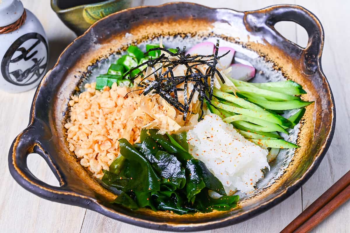 Hiyashi tanuki udon topped with tenkasu, okra, wakame, grated daikon, kamaboko, cucumber, katsuobushi and kizami nori side view