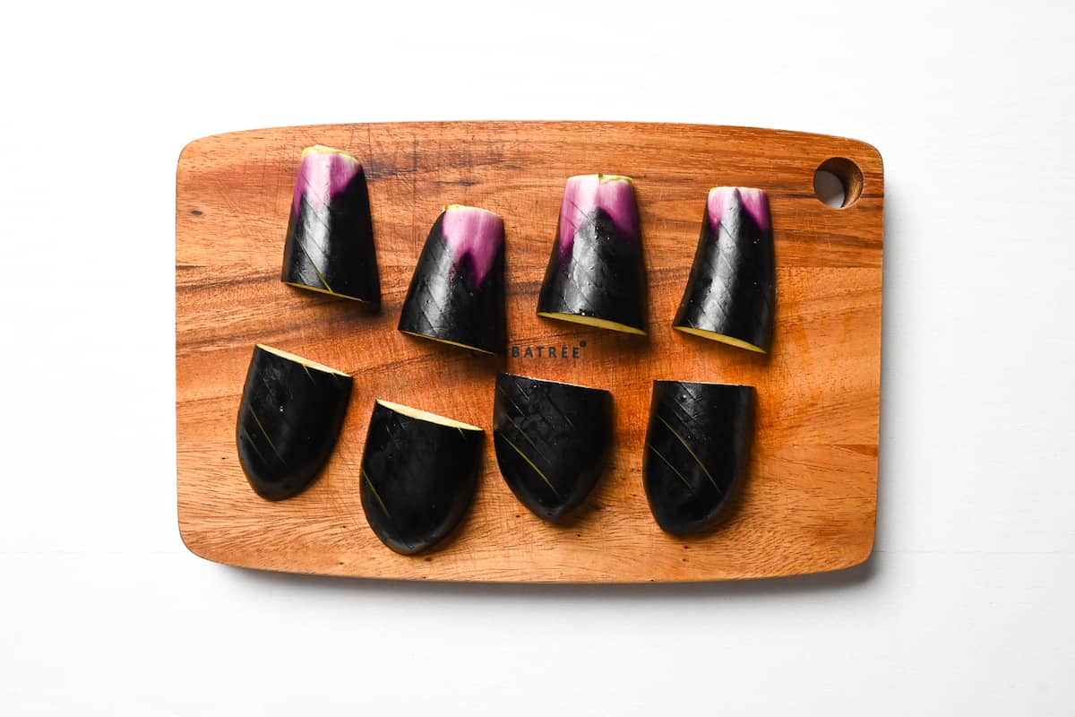 Eggplant cut in halves vertically and horizontally on a wooden chopping board