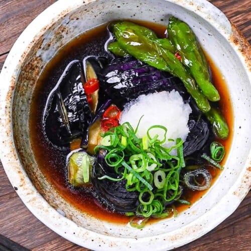 nasu no agebitashi served in a cream bowl and topped with grated daikon and chopped spring onion