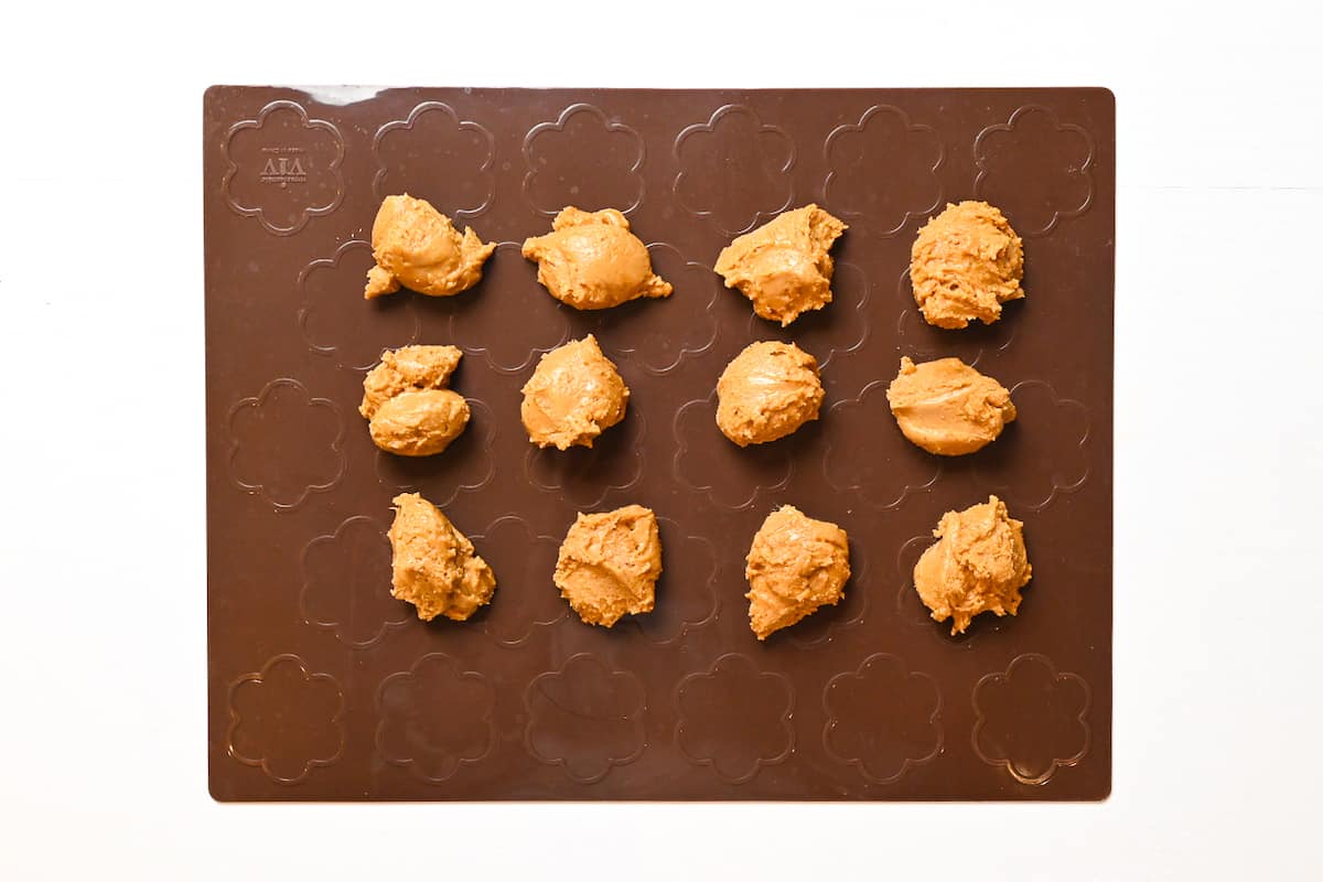 Sata Andagi dough divided into 12 equal pieces on a brown silicone baking mat