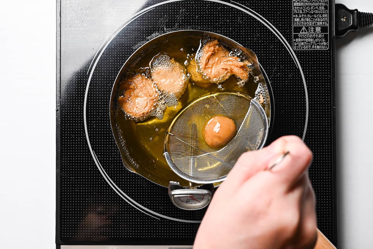 Sata andagi carefully placed in oil using a mesh spoon