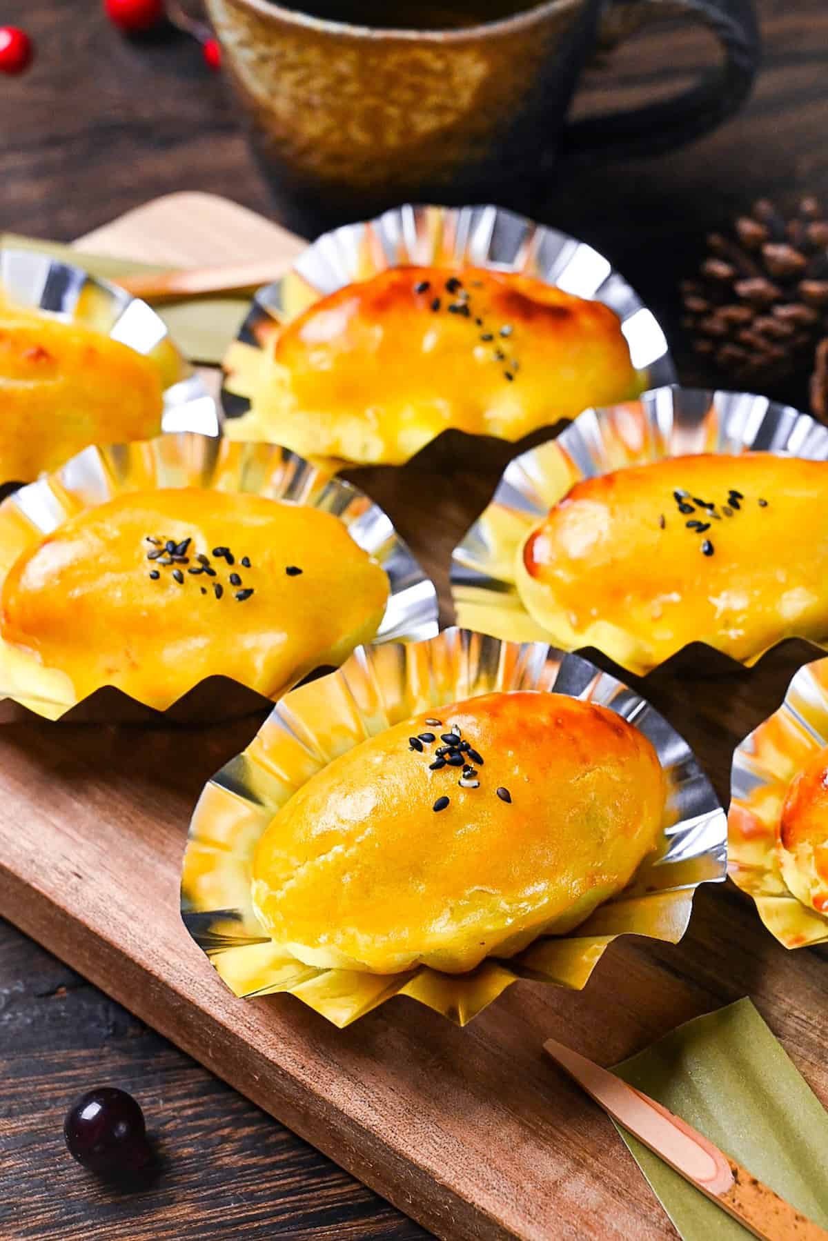 Japanese sweet potato dessert in foil cases sprinkled with black sesame seeds on a wooden chopping board