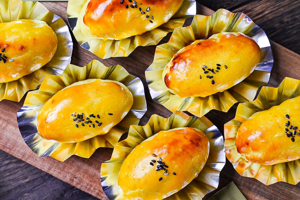 Japanese sweet potato dessert in foil cases sprinkled with black sesame seeds on a wooden chopping board top down view