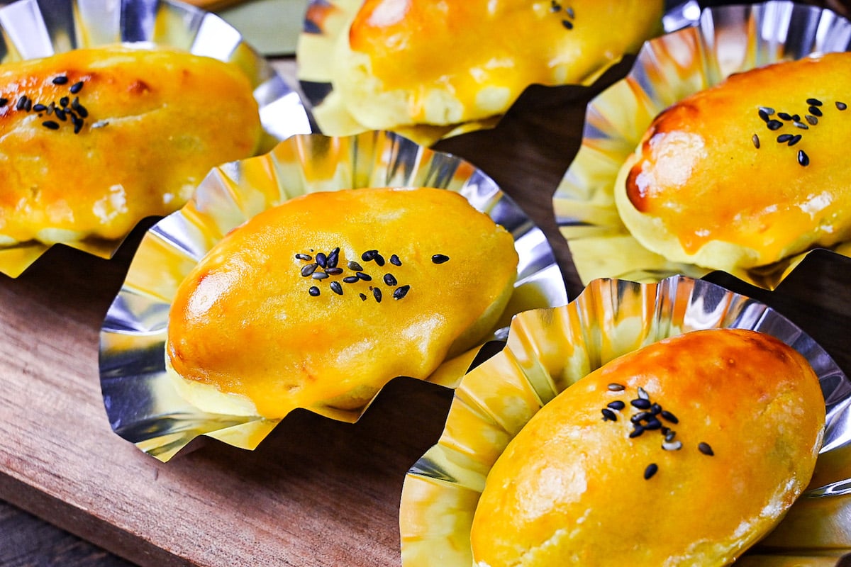 Japanese sweet potato dessert in foil cases sprinkled with black sesame seeds on a wooden chopping board