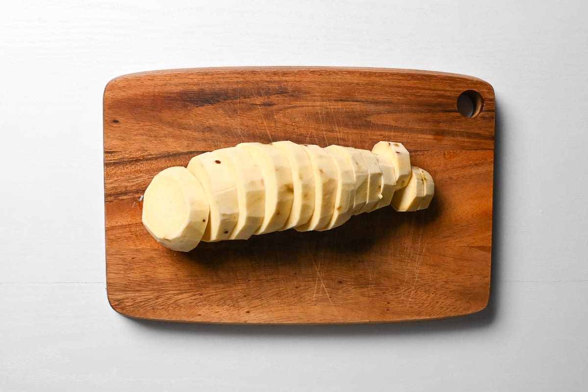 Peeled sweet potato cut into slices on a wooden chopping board