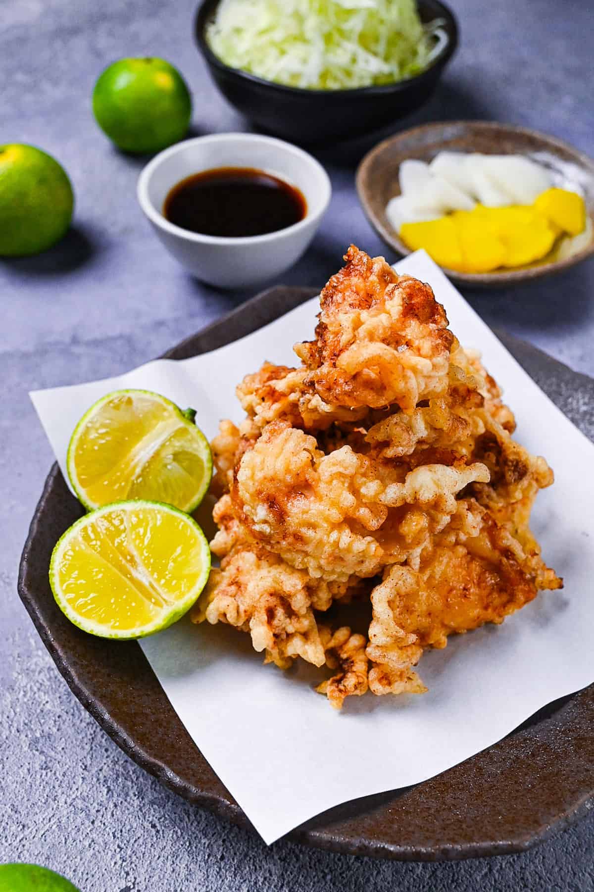toriten (chicken tempura) piled up on a brown plate with two halves of kabosu citrus