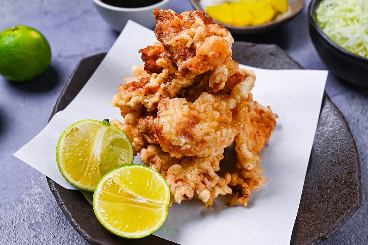 toriten (chicken tempura) piled up on a brown plate with two halves of kabosu citrus
