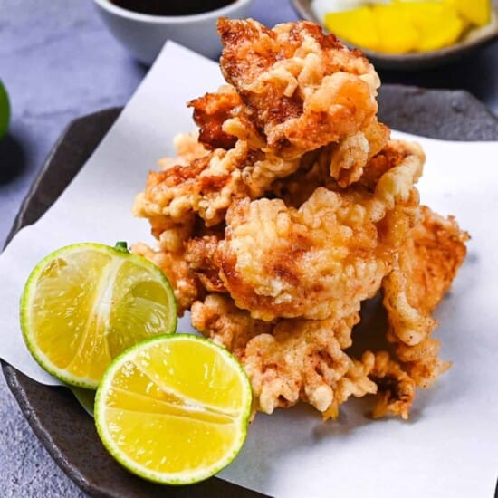 toriten (chicken tempura) piled up on a brown plate with two halves of kabosu citrus