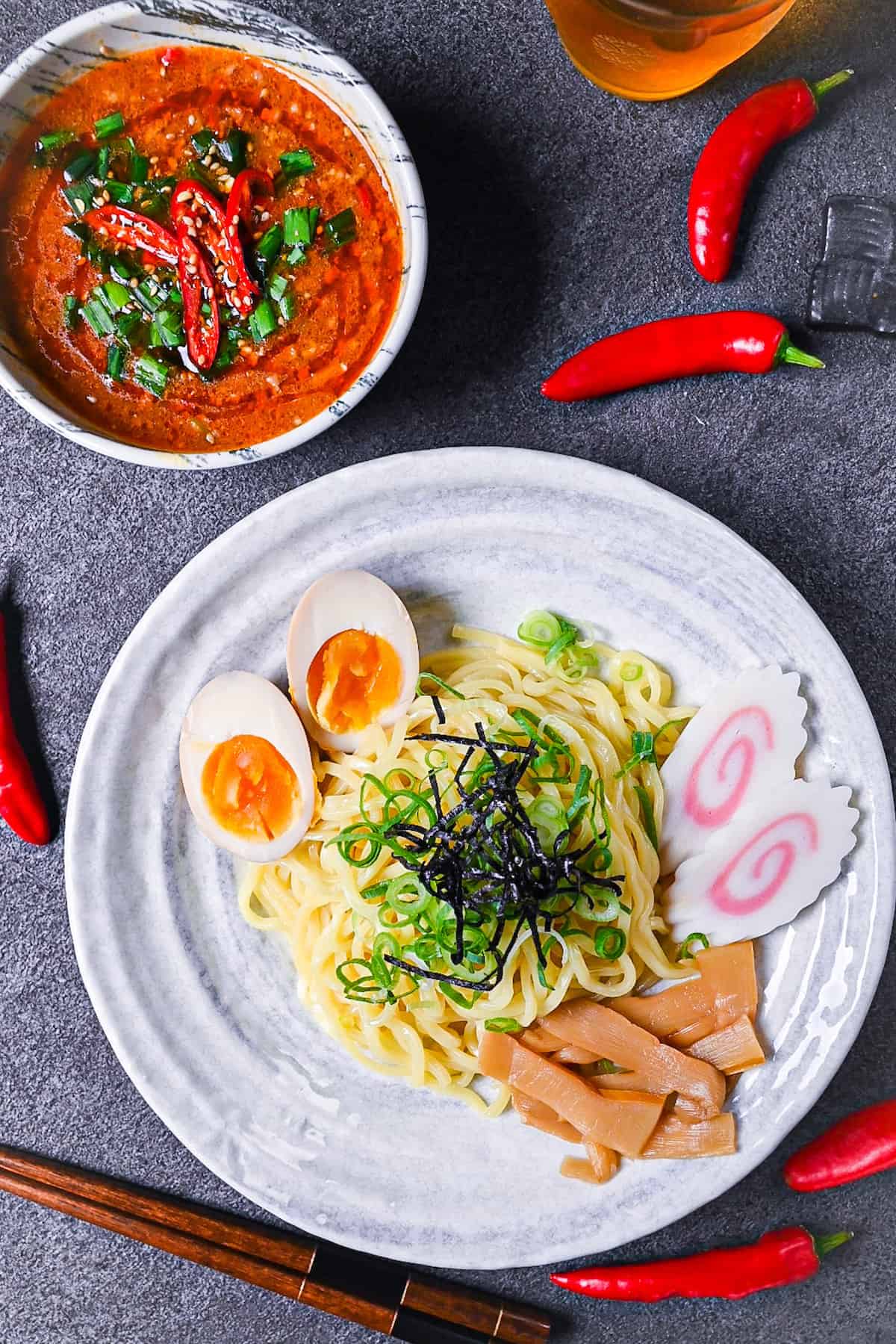 Japanese ramen noodles on a white plate with menma, narutomaki and ramen eggs served next to a bowl of spicy tsukemen soup