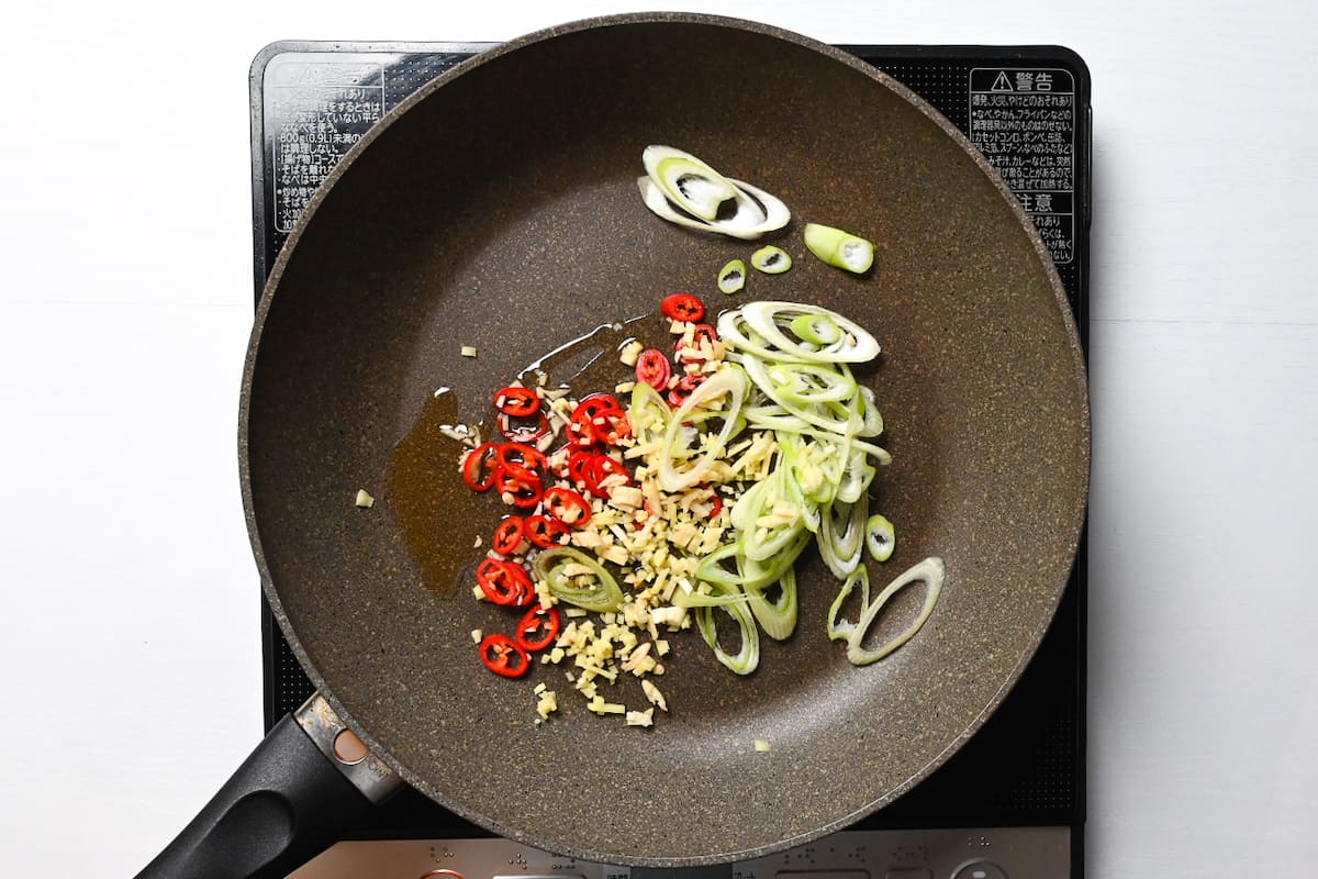 Frying chopped spring onion, chili, garlic and ginger in sesame oil