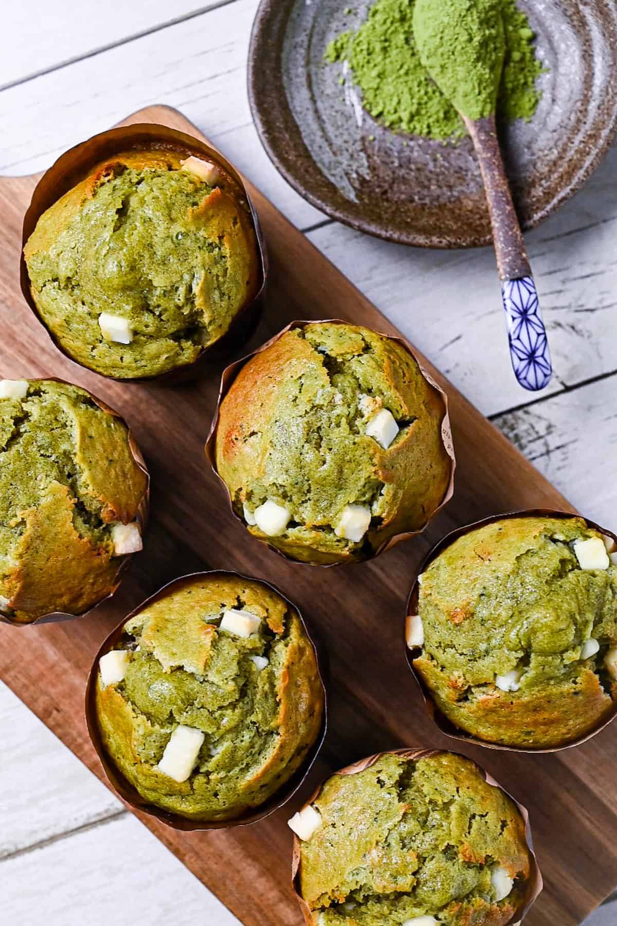 Matcha muffins with white chocolate chips on a wooden chopping board