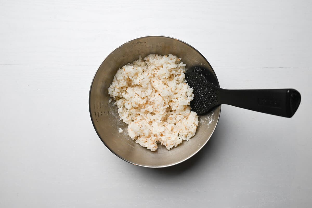 cooked rice mixed with sesame seeds and potato starch in a mixing bowl