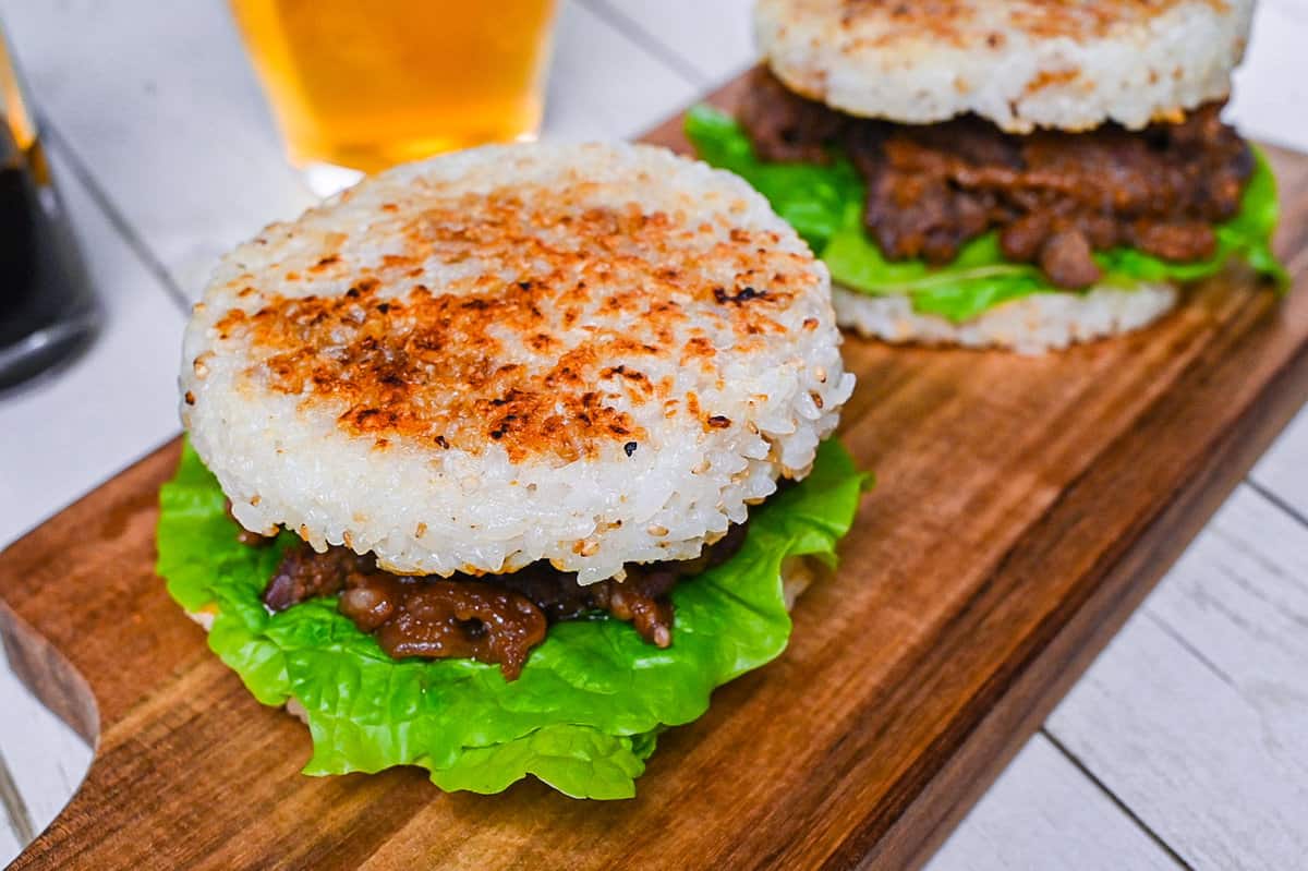 Yakiniku Rice Burger filled with frilly lettuce and yakiniku style pan fried beef on a wooden chopping board