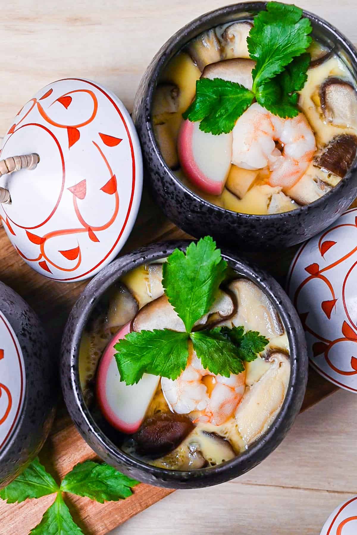 Chawanmushi (Japanese steamed egg custard) in black steaming cups with white and red decorative lids top down