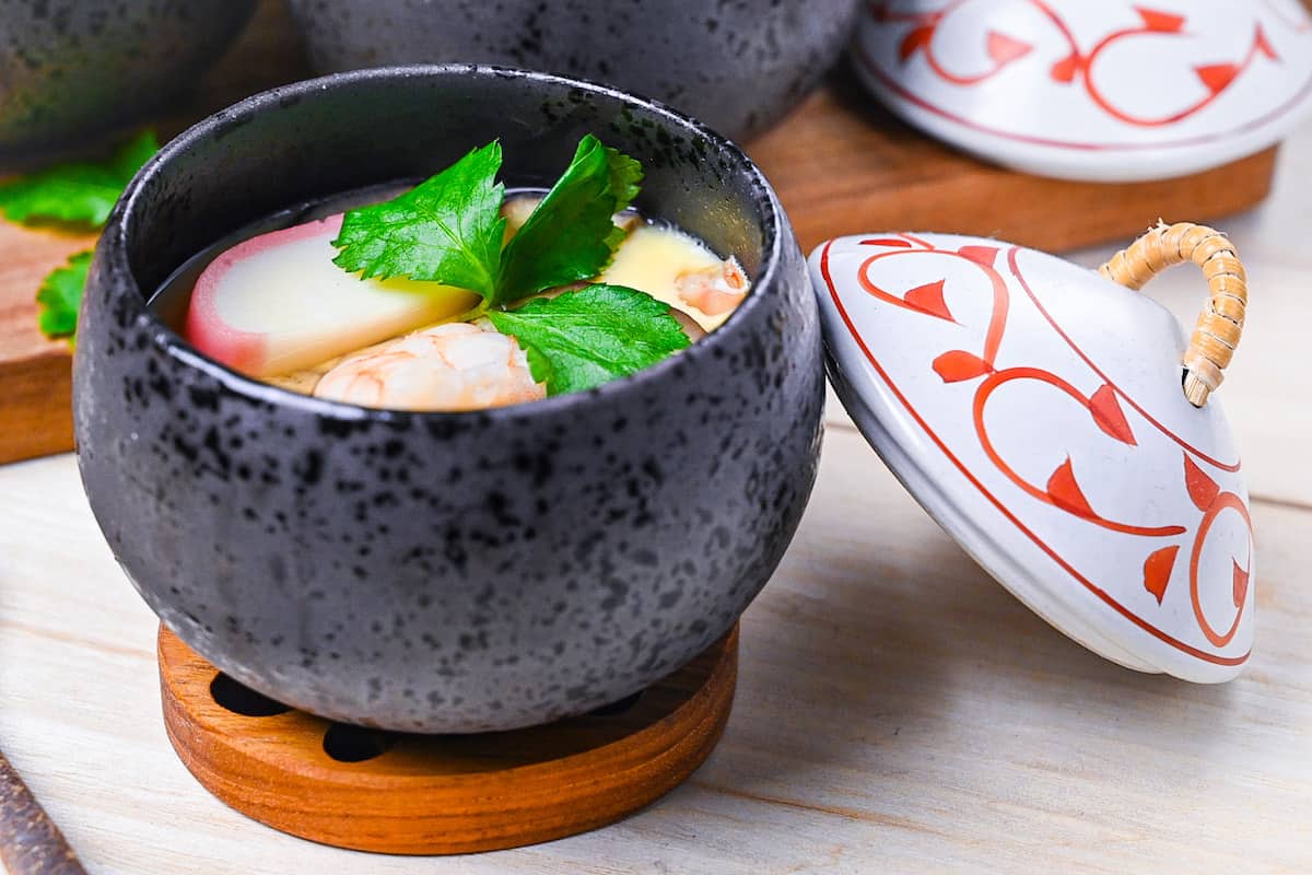 Chawanmushi (Japanese steamed egg custard) in black steaming cups with white and red decorative lids side angle