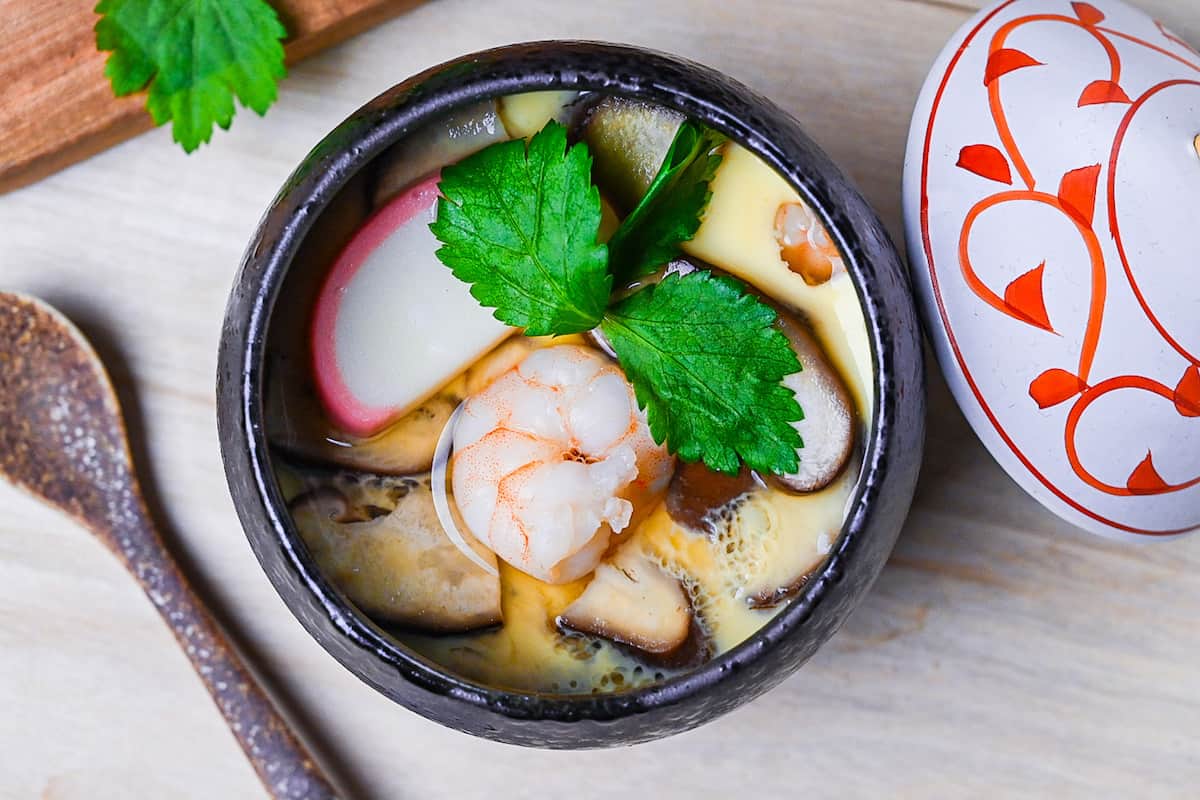 Chawanmushi (Japanese steamed egg custard) in black steaming cups with white and red decorative lids top down