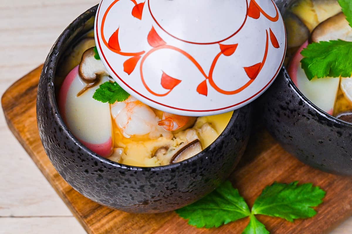 Chawanmushi (Japanese steamed egg custard) in black steaming cups with white and red decorative lids