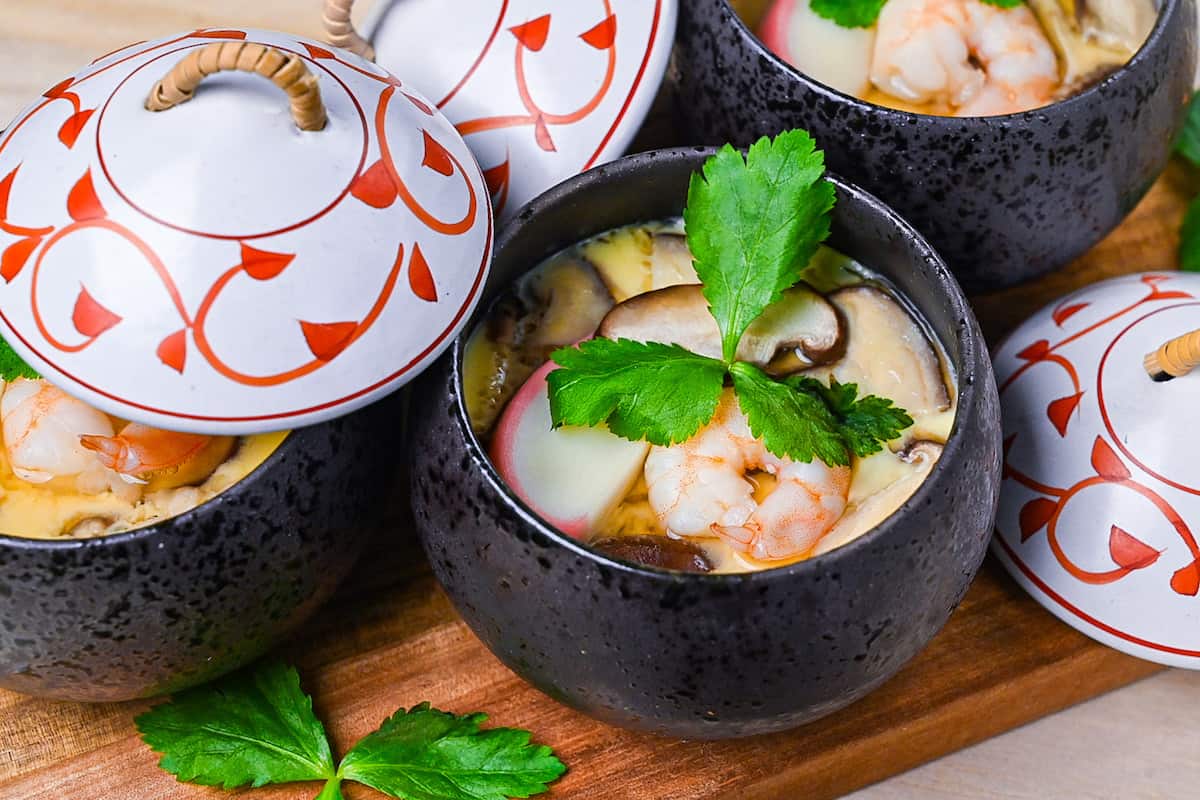 Chawanmushi (Japanese steamed egg custard) in black steaming cups with white and red decorative lids