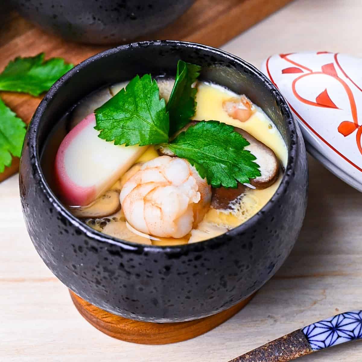 Chawanmushi (Japanese steamed egg custard) in black steaming cups with white and red decorative lids