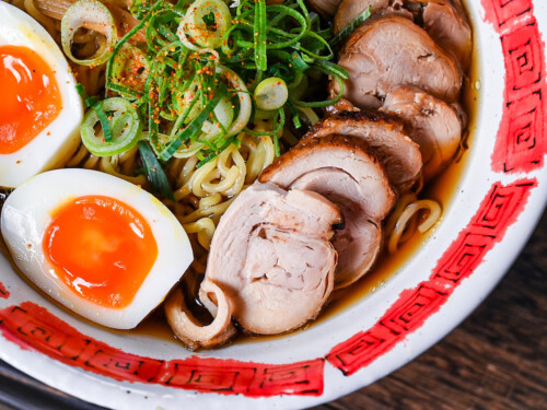 Homemade chicken chashu served on top of shoyu ramen in a white and red bowl close up