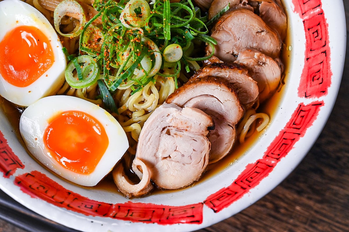 Homemade chicken chashu served on top of shoyu ramen in a white and red bowl close up