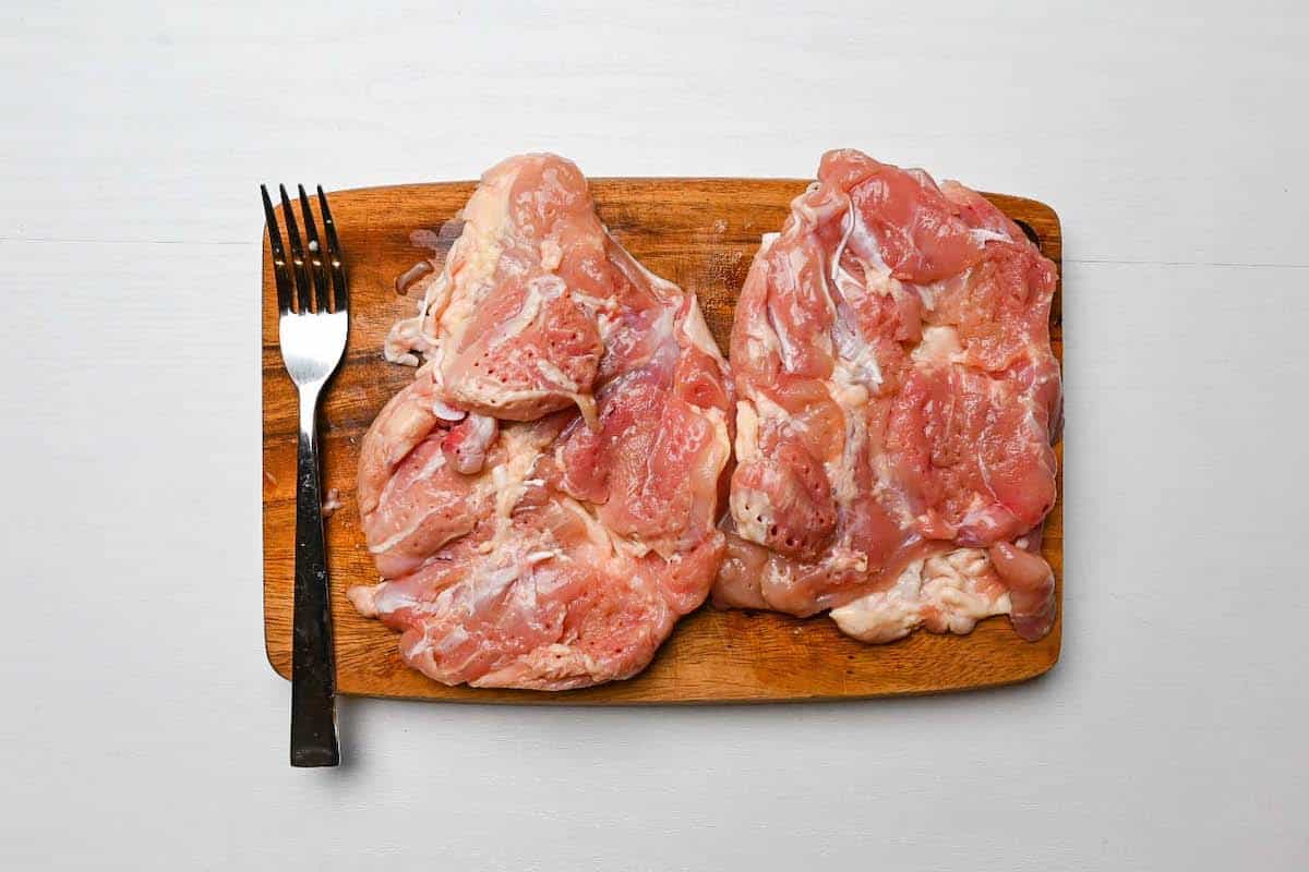 Chicken thigh pierced with a fork on a wooden chopping board