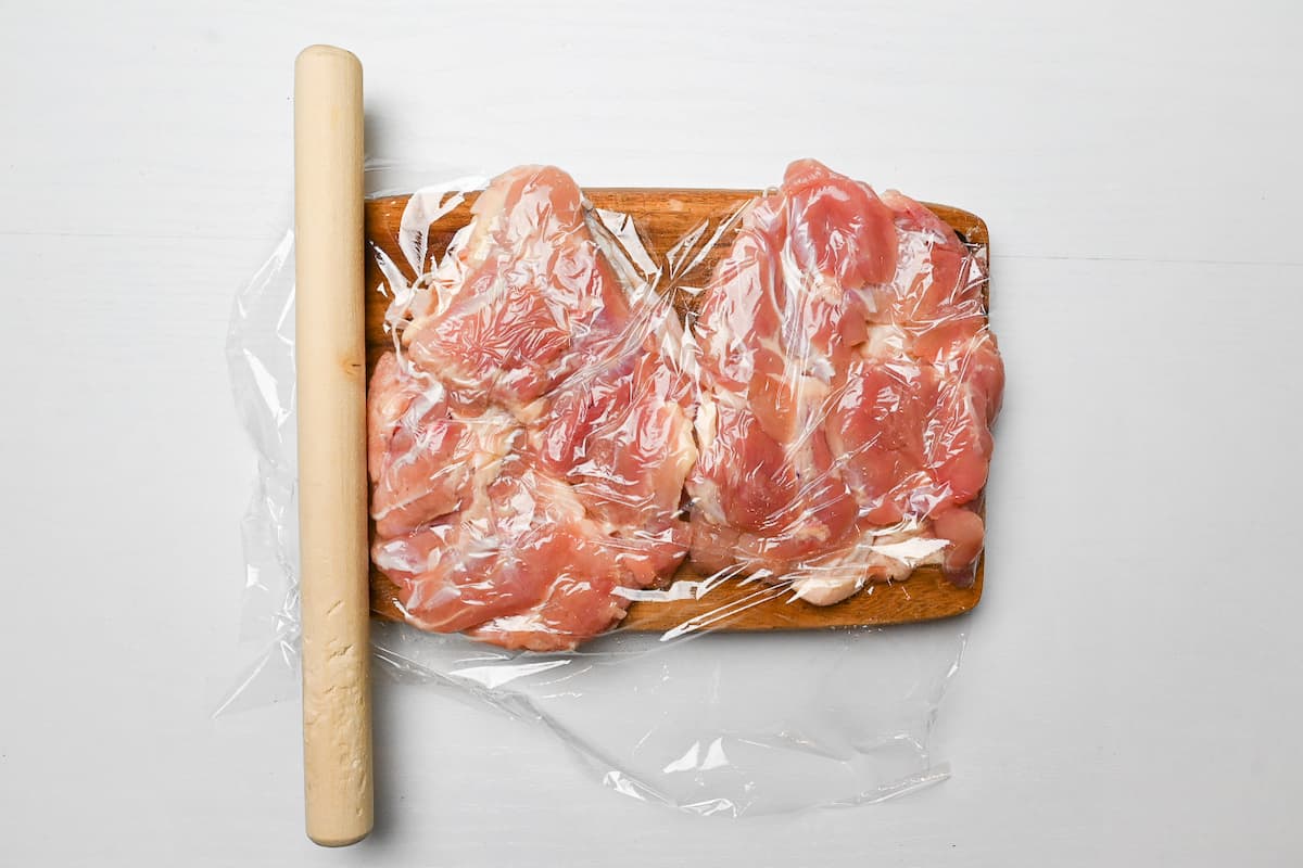 Chicken thigh covered with plastic wrap and flattened with a rolling pin