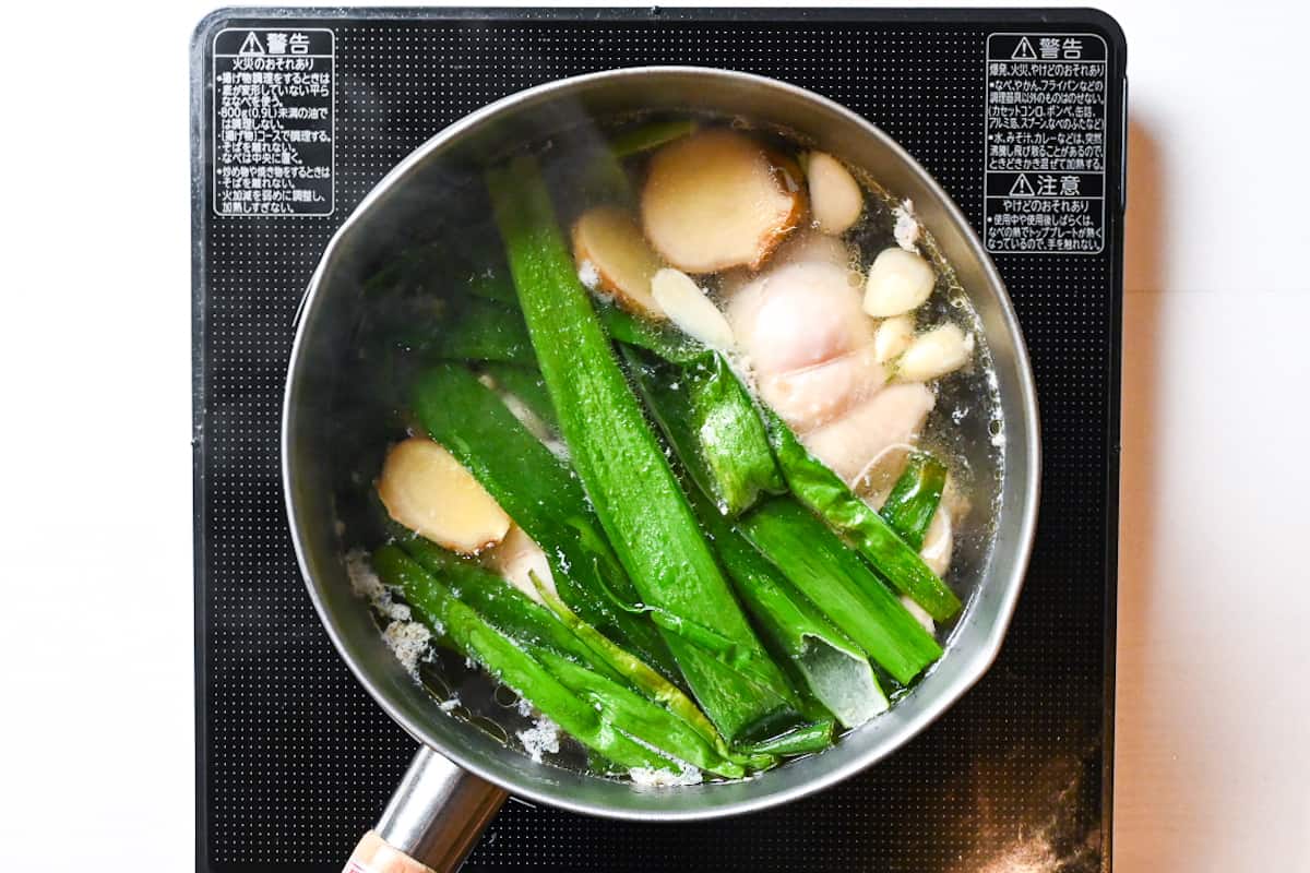 Rolled chicken thigh simmering in broth with ginger, garlic and spring onions