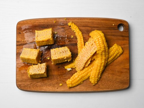 Corn cobs with the kernels removed and core cut into quarters on a wooden chopping board