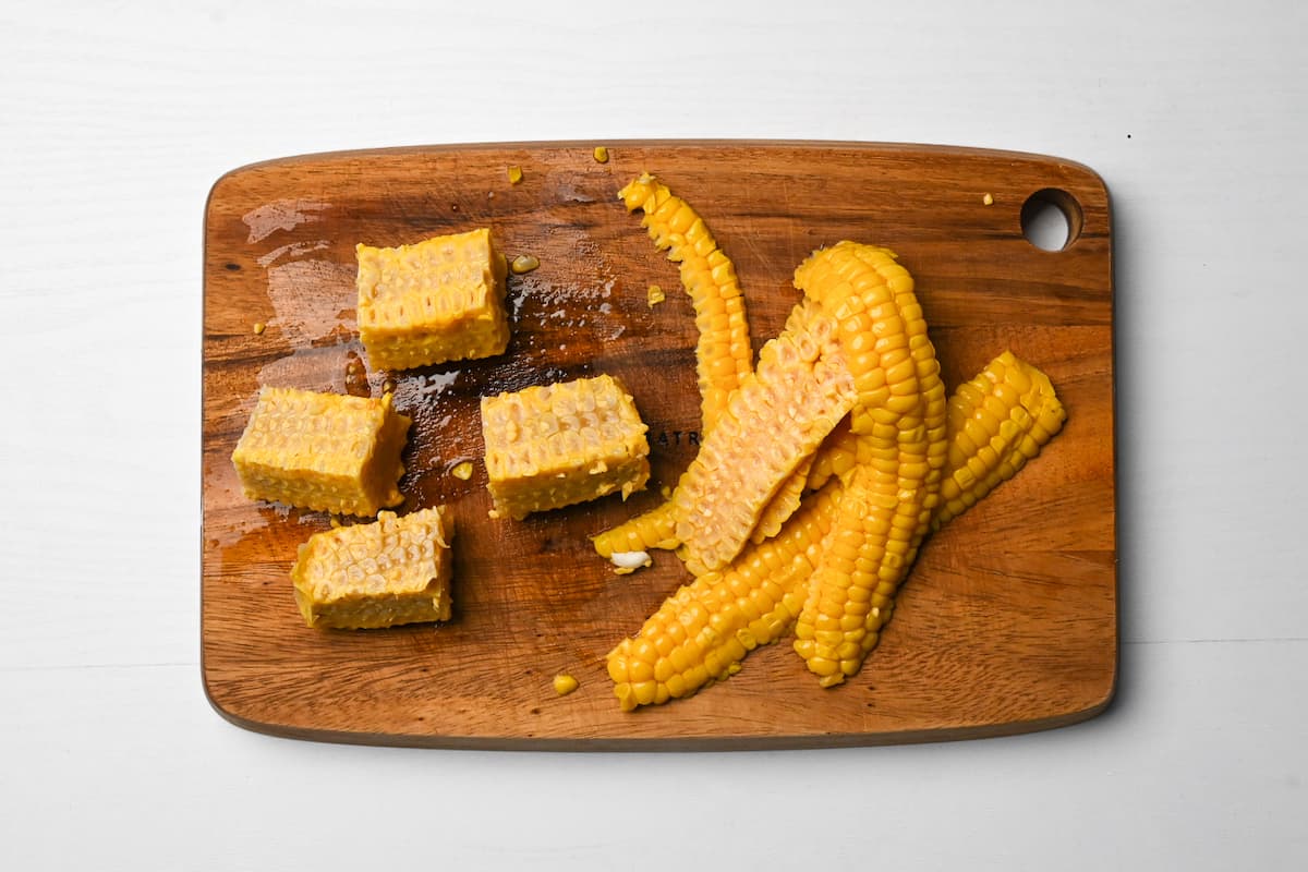Corn cobs with the kernels removed and core cut into quarters on a wooden chopping board
